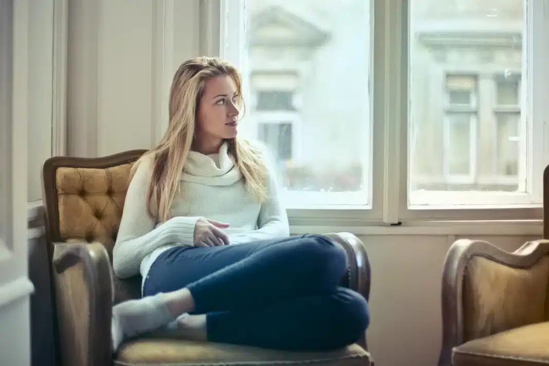 Žena sedi na fotelji i gleda kroz prozor