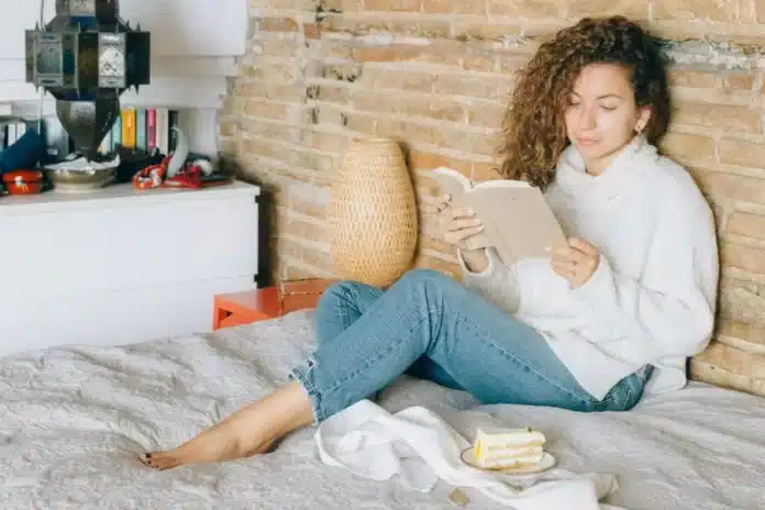 Žena sedi na krevetu i čita knjigu