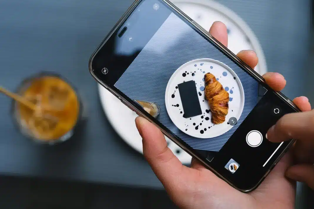 Ruke drže telefon i slikaju kroasan postavljen na tanjiru